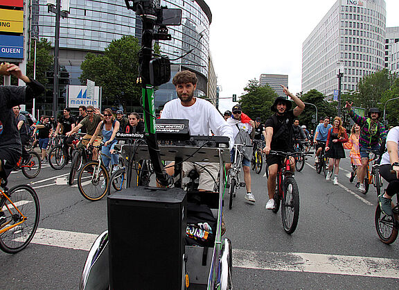 Mann in weißem T-Shirt auf Lastenrad umgeben von vielen fröhlichen Radfahrenden